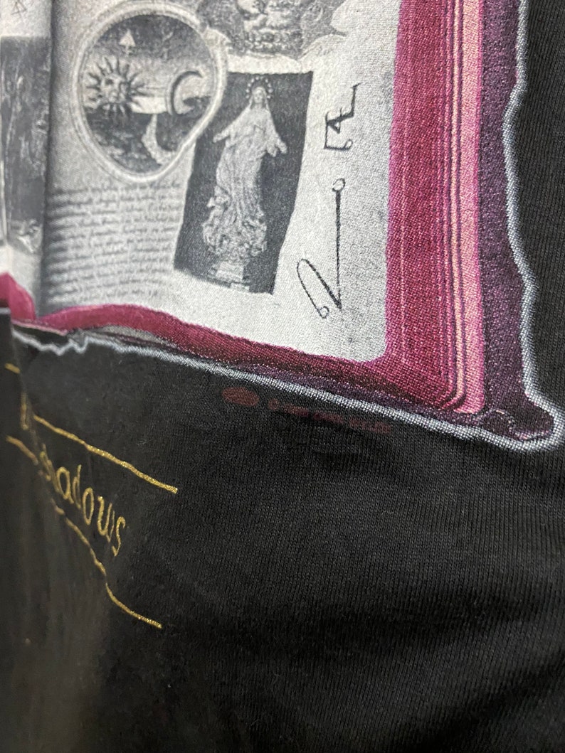 Puede incluir: Una camiseta negra con un gr&aacute;fico dorado de un libro con im&aacute;genes y el texto "The Shadows".