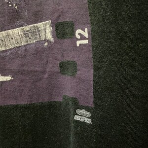 Pu&ograve; includere: Maglietta nera con una grafica viola e bianca di una pellicola con il numero 12 stampato su di essa. La grafica include anche il testo "Nintendo" e "High-Impact".