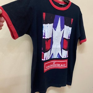 May include: A black t-shirt with a red ringer. The shirt features a graphic of a white star on a red, blue, and white background. The text "RADIOHEAD" is printed in red on a white rectangle below the graphic.