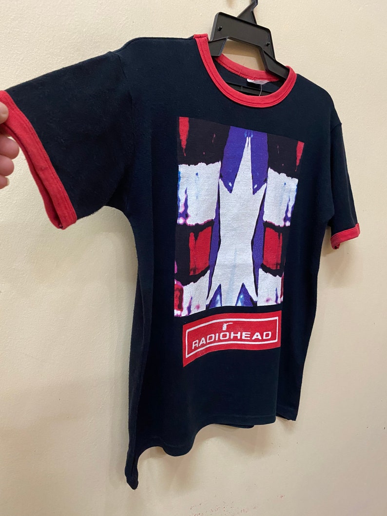May include: A black t-shirt with a red ringer. The shirt features a graphic of a white star on a red, blue, and white background. The text "RADIOHEAD" is printed in red on a white rectangle below the graphic.