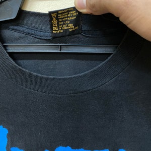 May include: Black t-shirt with a blue graphic print of the word "Insanity". The tag on the shirt reads "100% Cotton, Machine Wash Medium 40&deg;C 100&deg;F, Do Not Bleach, Dry Low, Do Not Iron If Decorated, RN 69761, CA12280".