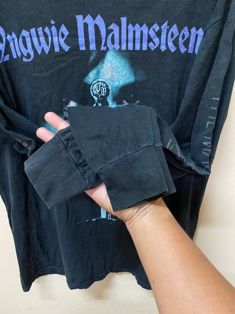 May include: Black long-sleeved t-shirt with a faded image of a person and the text "Yngwie Malmsteen" in purple lettering.