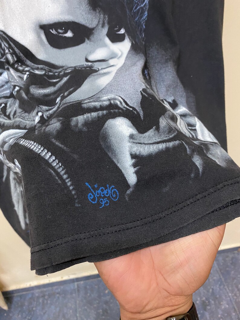 May include: Black t-shirt with a graphic print of a person's face. The print is in shades of gray and white. The t-shirt has a blue signature that says "Viagra 95".