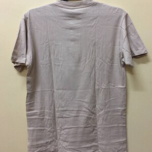 Puede incluir: Una camiseta lisa de color beige claro con mangas cortas y cuello redondo.