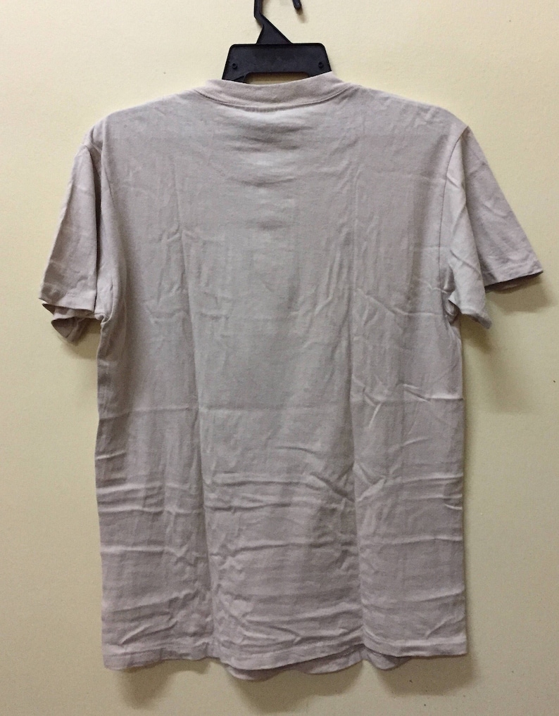 Puede incluir: Una camiseta lisa de color beige claro con mangas cortas y cuello redondo.