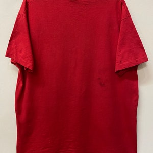 May include: A plain red t-shirt with short sleeves. The shirt is hanging on a hanger.