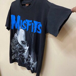 May include: Black t-shirt with a blue "Misfits" graphic and a black and white image of a person with a skull face.