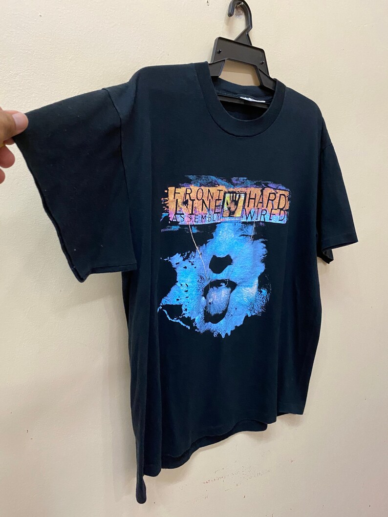 May include: Black t-shirt with a graphic print of a blue and purple mouth with a tongue sticking out. The text "FRONT LINE HARD ASSEMBLY WIRED" is printed on the shirt.