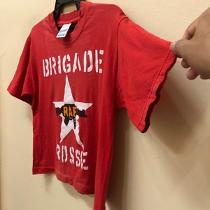 Pu&ograve; includere: Maglietta rossa a maniche corte con una stella bianca e il testo "BRIGADE RAF RUSSE" stampato sul davanti.