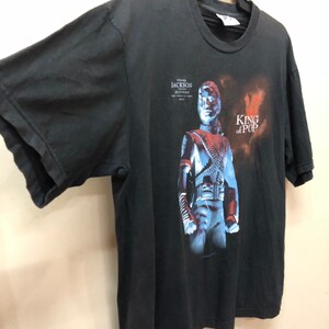 May include: Black t-shirt with a graphic print of Michael Jackson from his "History" album. The text "King of Pop" is printed on the shirt.