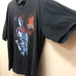 May include: Black t-shirt with a faded image of Michael Jackson in a silver jacket and the text "King of Pop".