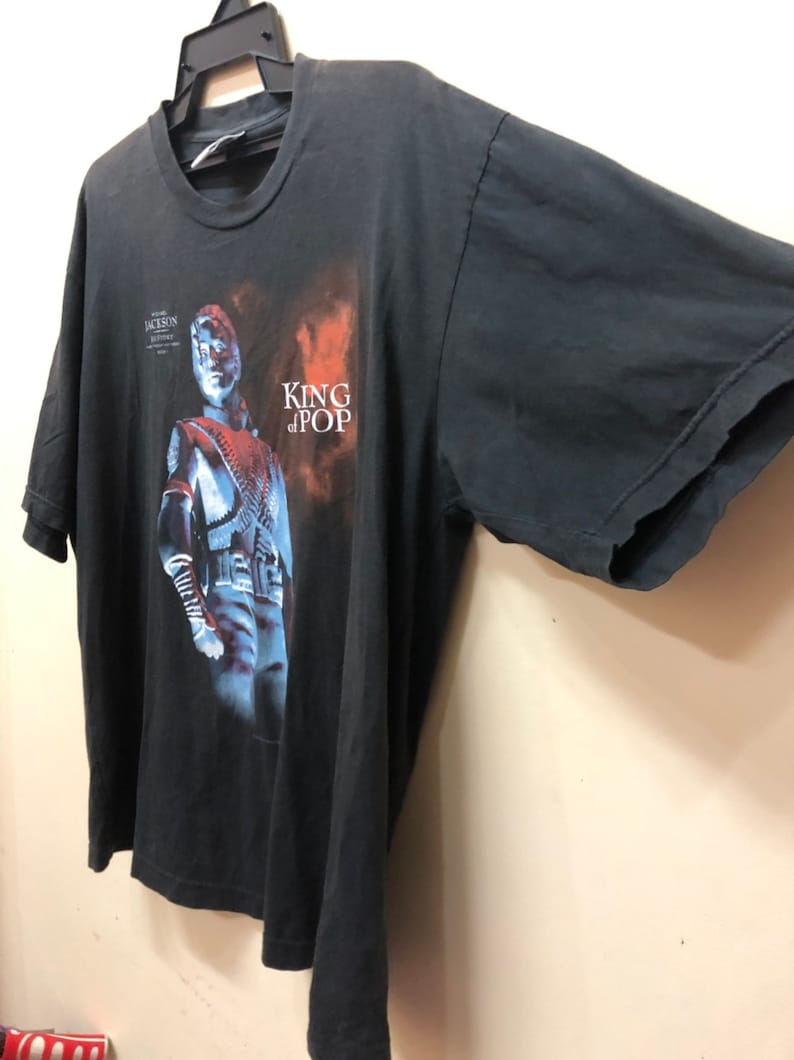 May include: Black t-shirt with a faded image of Michael Jackson in a silver jacket and the text "King of Pop".
