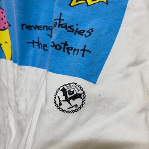 Puede incluir: Camiseta blanca con un gr&aacute;fico azul y verde de figuras de palitos. El texto "revenge fantasies the potent" est&aacute; escrito en negro. La parte inferior de la camiseta tiene un logotipo en blanco y negro que dice "Alternative Tentacles".