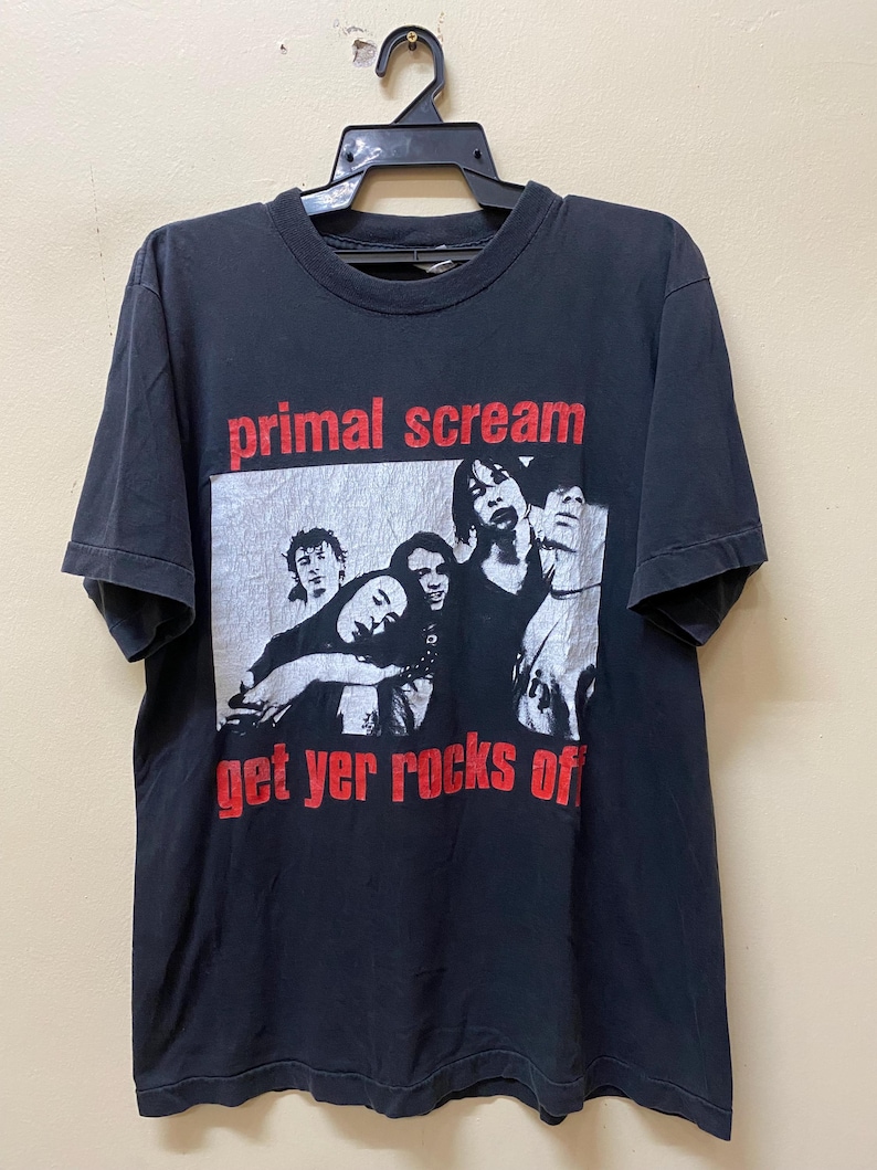 May include: Black t-shirt with a band graphic. The graphic features a black and white photo of a band with the text "primal scream get yer rocks off" in red.