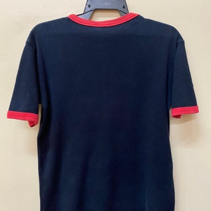 May include: A black t-shirt with red trim around the neck and sleeves. The shirt is hanging on a black hanger.