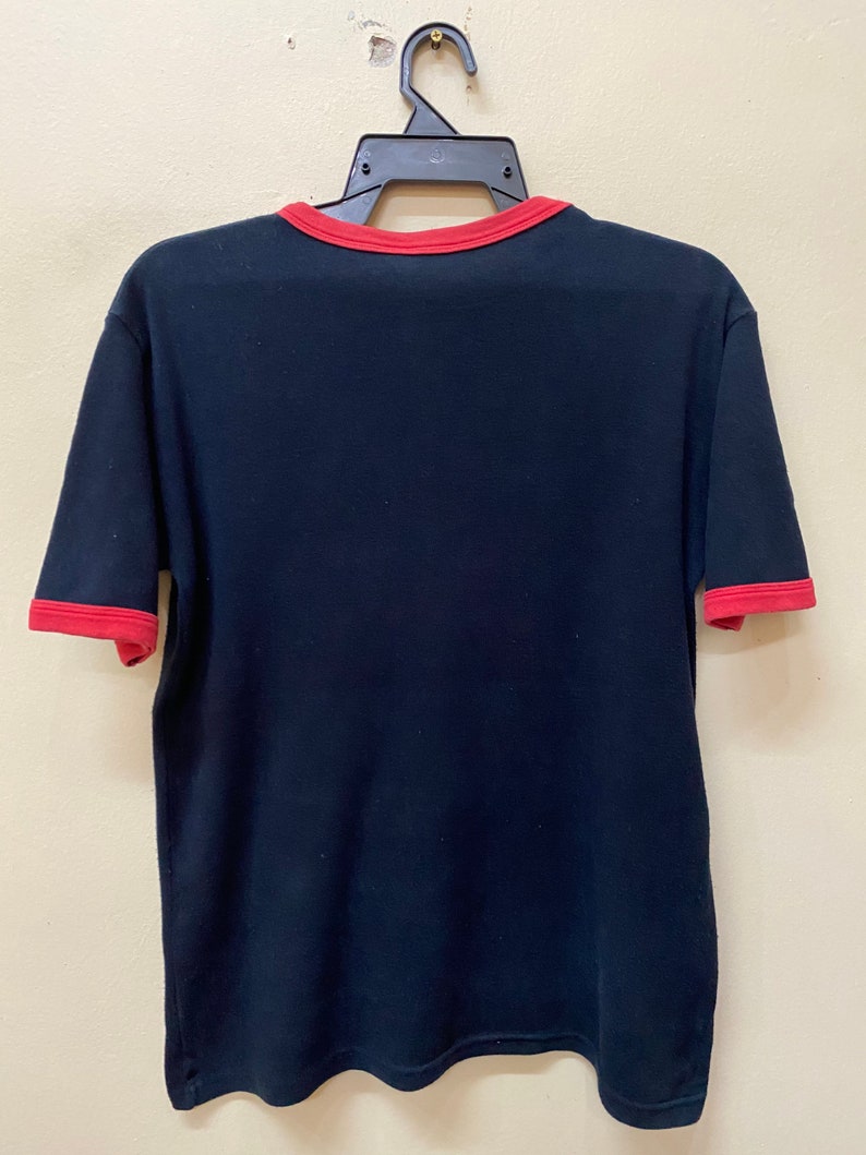 May include: A black t-shirt with red trim around the neck and sleeves. The shirt is hanging on a black hanger.