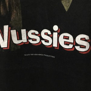 May include: Black t-shirt with white text that reads "Vussies" in a bold, red outlined font. The text is centered on the shirt and is accompanied by the text "TM & &copy; 1999 VIEW ASKEW PRODUCTIONS" in a smaller, white font below.