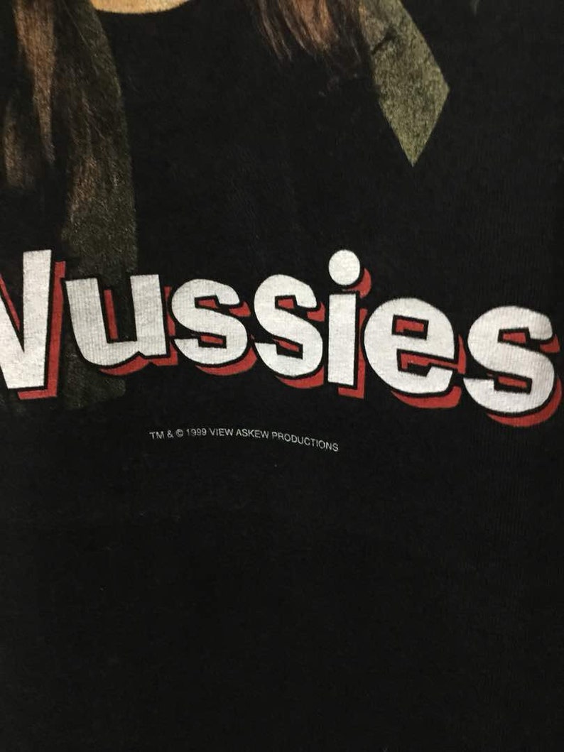 May include: Black t-shirt with white text that reads "Vussies" in a bold, red outlined font. The text is centered on the shirt and is accompanied by the text "TM & &copy; 1999 VIEW ASKEW PRODUCTIONS" in a smaller, white font below.