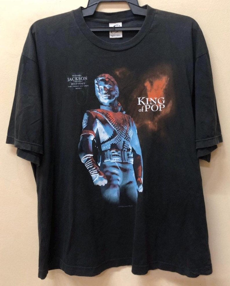 May include: Black t-shirt with a graphic of Michael Jackson from his "HIStory" album. The graphic features a blue and red image of Michael Jackson with the text "King of Pop".