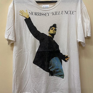 Puede incluir: Camiseta blanca con una imagen en blanco y negro de Morrissey, el cantante, con el texto "MORRISSEY "KILL UNCLE"" impreso en la parte delantera.