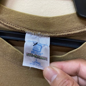 K&ouml;nnte beinhalten: Ein braunes Langarmshirt mit einem wei&szlig;en Etikett, auf dem "Belton Dye-Namic" und "L Long Made in U.S.A." steht.
