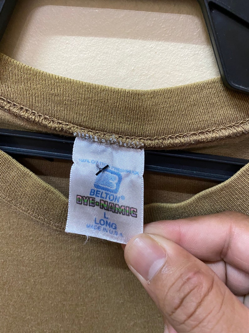 K&ouml;nnte beinhalten: Ein braunes Langarmshirt mit einem wei&szlig;en Etikett, auf dem "Belton Dye-Namic" und "L Long Made in U.S.A." steht.
