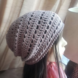 May include: A light grey crocheted beanie with a lacy pattern. The beanie is worn on a mannequin with long dark hair.