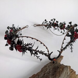 Peut inclure: Couronne florale noire avec des fleurs rouges et des cornes noires. La couronne est faite de fil de fer et a un design perl&eacute;.
