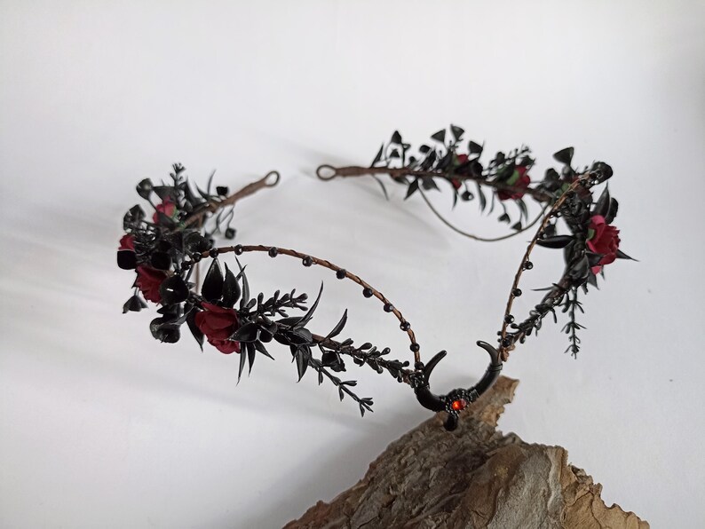 Peut inclure: Couronne florale noire avec des fleurs rouges et des cornes noires. La couronne est faite de fil de fer et a un design perl&eacute;.