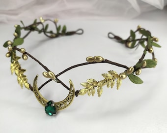 May include: A gold leaf and twig crown with a crescent moon charm and a green gemstone. The crown is decorated with small gold beads.