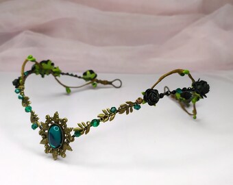 May include: A delicate gold wire headband with black roses, green leaves, and emerald green gemstones. The headband is adorned with a large, ornate, bronze pendant with a green gemstone in the center.
