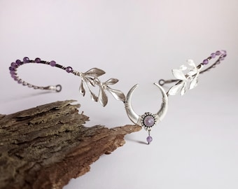 Può includere: Fascia per capelli in argento con un design a mezzaluna e una pietra preziosa di ametista. La fascia è decorata con accenti di foglie d'argento e presenta una pietra preziosa di ametista viola.