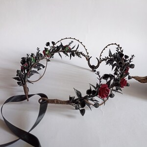 Peut inclure: Couronne florale noire avec des roses rouges et des feuilles noires. La couronne est faite de fil de fer et a un ruban noir.