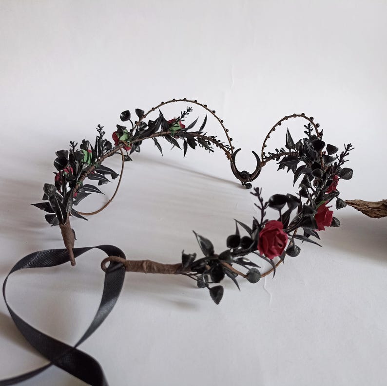 Peut inclure: Couronne florale noire avec des roses rouges et des feuilles noires. La couronne est faite de fil de fer et a un ruban noir.