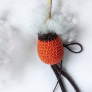 May include: Orange crocheted ball with brown trim, filled with white stuffing and attached to brown yarn.