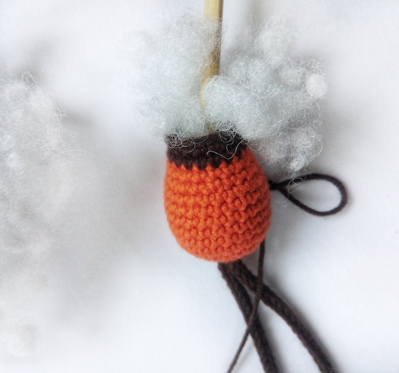 May include: Orange crocheted ball with brown trim, filled with white stuffing and attached to brown yarn.