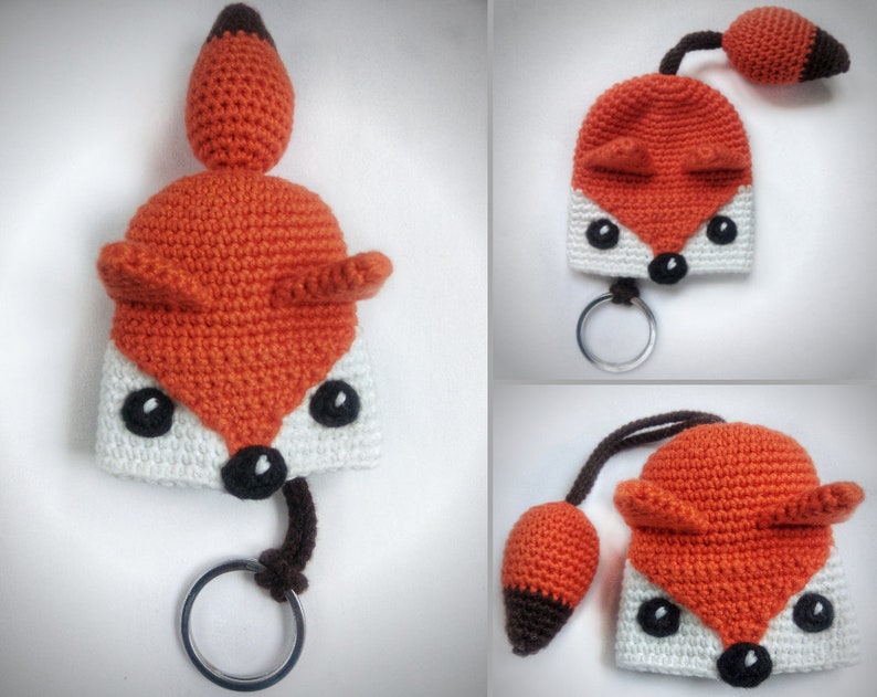 May include: A crocheted fox keychain with a white and orange body, black eyes, and a brown tail. The fox is attached to a silver key ring.