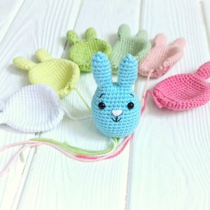 May include: A blue crocheted bunny with black eyes and a white nose, surrounded by crocheted shapes in various colors, including green, yellow, pink, and white.