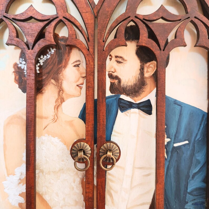 May include: A painted portrait of a couple in a wooden frame with a carved design. The woman is wearing a white dress and the man is wearing a blue suit with a white shirt and a black bow tie. They are looking at each other.