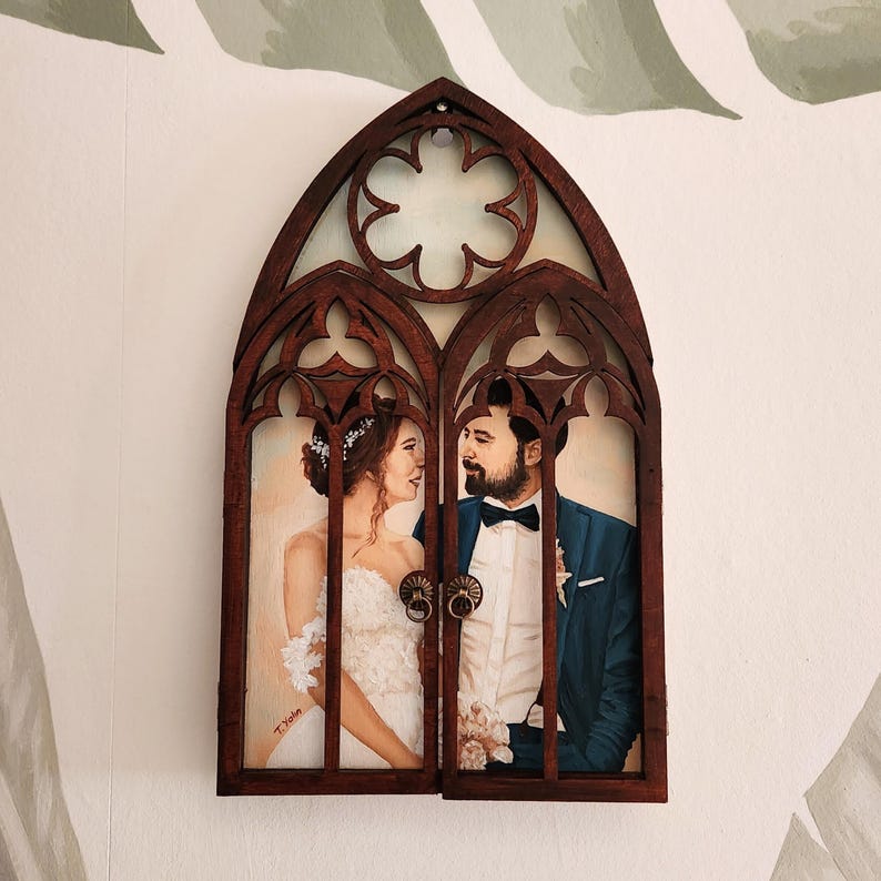 May include: A wooden frame with a gothic arch design, featuring a painted portrait of a couple. The couple is looking at each other and smiling. The frame is painted in a dark brown color and has a distressed finish.