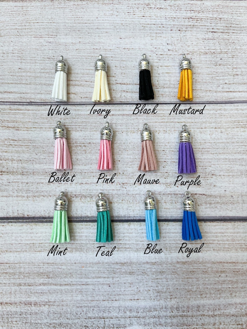 May include: Assortment of 12 tassel charms in various colors, including white, ivory, black, mustard, ballet pink, pink, mauve, purple, mint, teal, blue, and royal blue. Each tassel charm has a silver metal top.