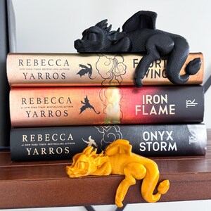 May include: Three fantasy novels with dragon bookends. The top book is "Fort Wing" by Rebecca Yarros. The middle book is "Iron Flame" by Rebecca Yarros. The bottom book is "Onyx Storm" by Rebecca Yarros. The bookends are black and gold dragons.
