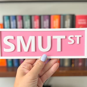Peut inclure: Une pancarte rose avec des lettres blanches qui indiquent "SMUT ST".