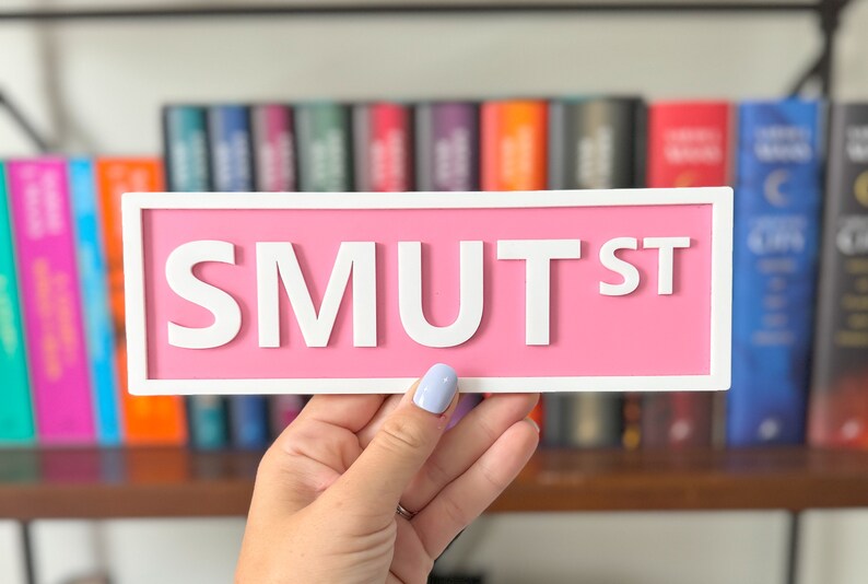 Peut inclure: Une pancarte rose avec des lettres blanches qui indiquent "SMUT ST".