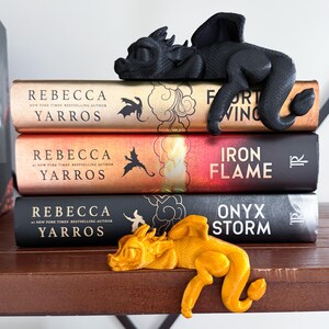 May include: Three hardcover books with black and gold dragon bookends. The books are titled "Fort Wing", "Iron Flame", and "Onyx Storm" and are all by Rebecca Yarros.