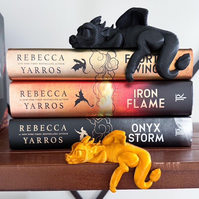 May include: Three hardcover books with black and gold dragon bookends. The books are titled "Fort Wing", "Iron Flame", and "Onyx Storm" and are all by Rebecca Yarros.