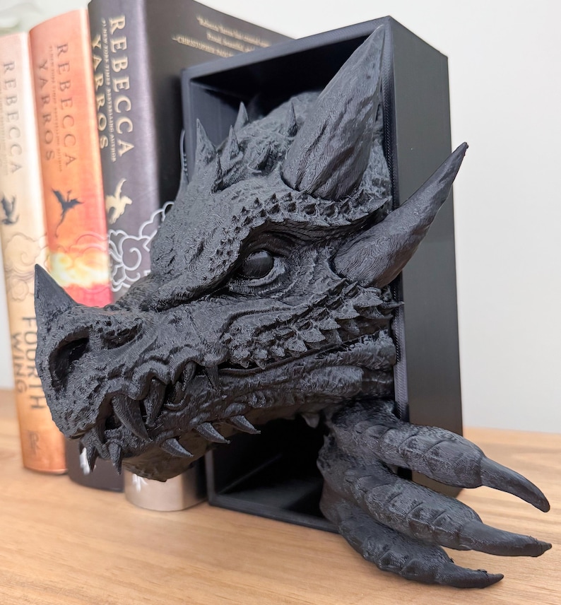 May include: Black dragon head bookend with sharp teeth and claws. The dragon head is mounted in a black frame and is a 3D printed sculpture.