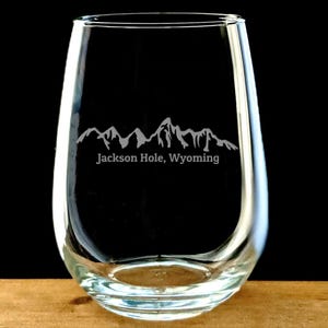 May include: A clear glass stemless wine glass with an etched design of mountains and the text "Jackson Hole, Wyoming".