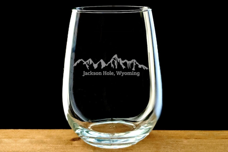 May include: A clear glass stemless wine glass with an etched design of mountains and the text "Jackson Hole, Wyoming".