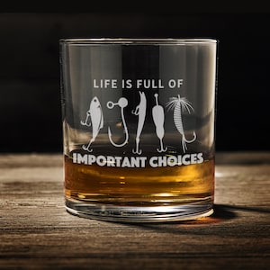 May include: A clear glass tumbler with the text "Life is full of important choices" and a row of fishing lures etched on the side. The tumbler is filled with amber liquid.